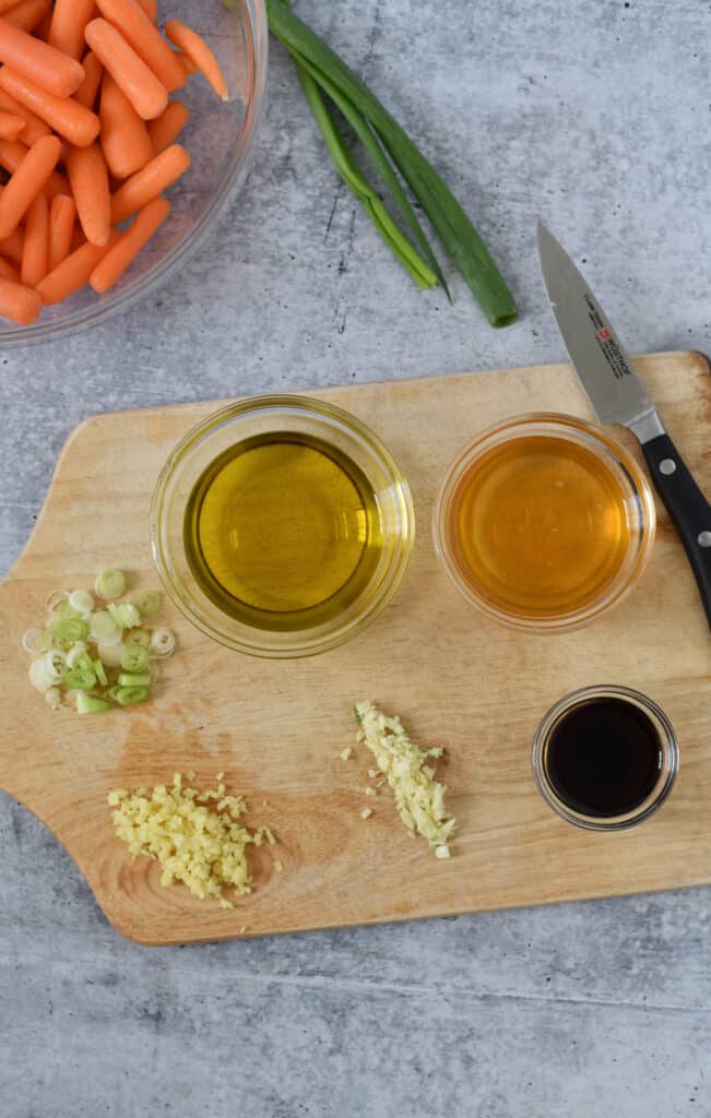 wooden cutting board with glass bowls of honey, soy sauce, olive oil, minced ginger, minced garlic and green onions