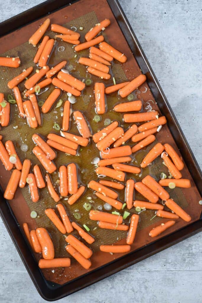baking tray with baby carrots covered in honey ginger sauce