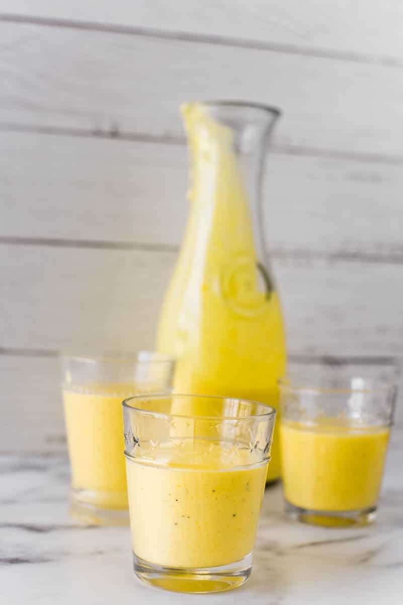 three glasses with mango lassi beside pitcher 
