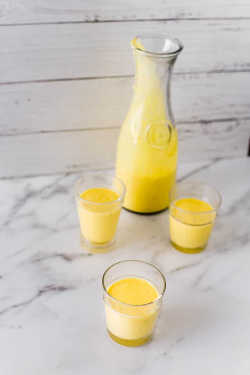 mango lassi in three glasses beside pitcher 