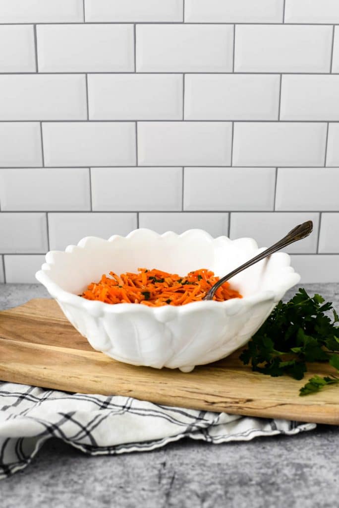 white bowl filled with french carrot salad on wooden board
