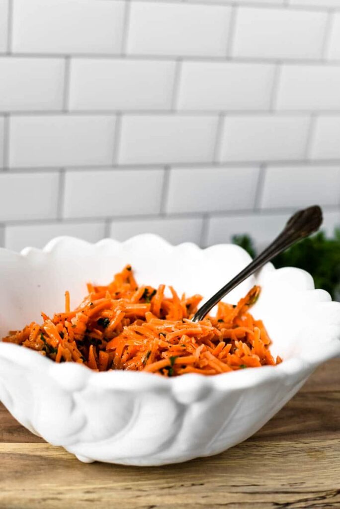 french carrot salad ready to be served in white bowl with spoon 