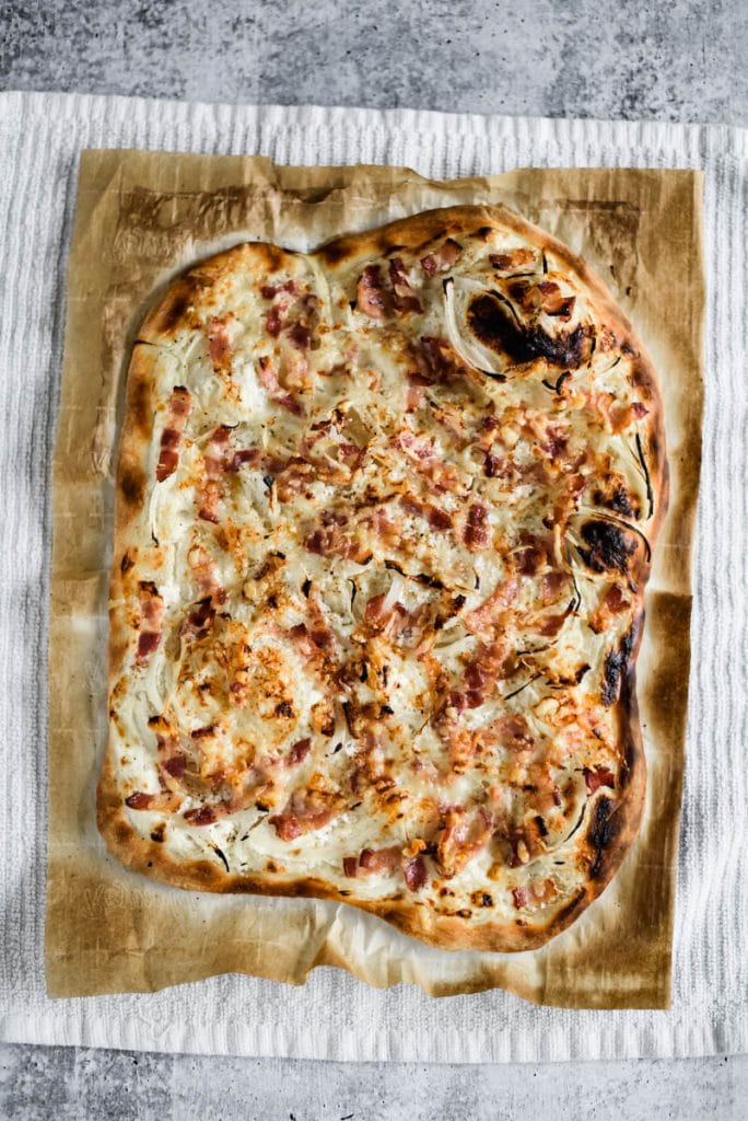 reshly baked tarte flambeed on parchment paper resting on white kitchen towel 