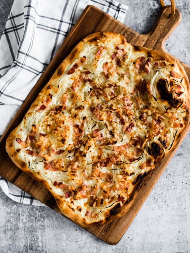 tarte flambée on wooden cutting board beside kitchen towel