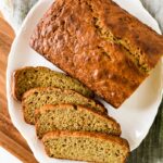 loaf of sourdough banana bread on white platter with four cut slices beside it