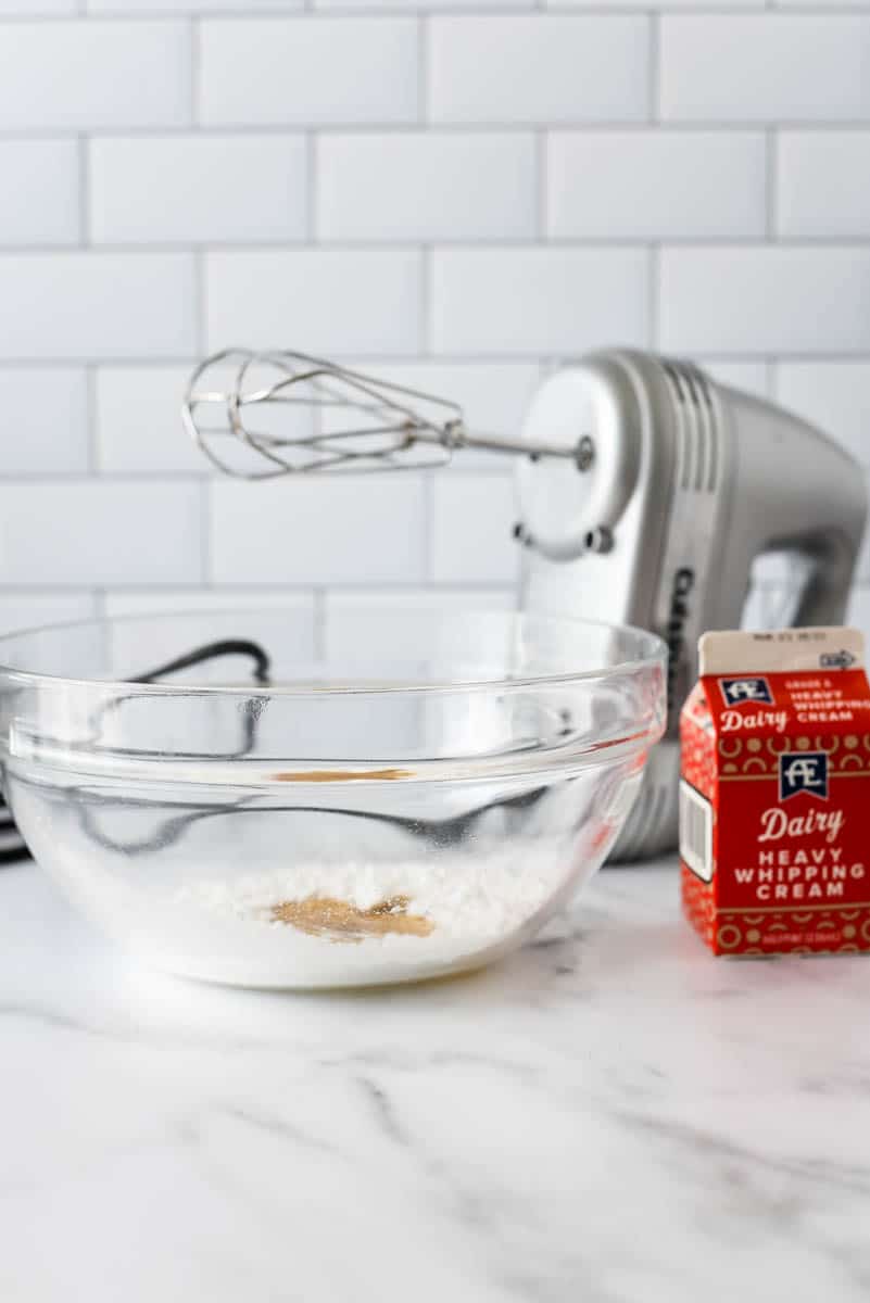 bowl with ingredients to make whipped cream next to handheld mixer