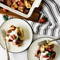 two plates with strawberry bread pudding sitting beside stoneware baking dish filled with more