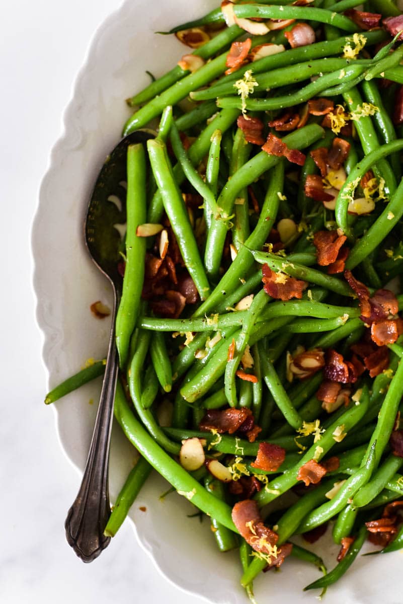 close up of green beans with bacon in white platter