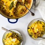 two plates piled with bobotie with forks on the side, next to serving dish with spoon