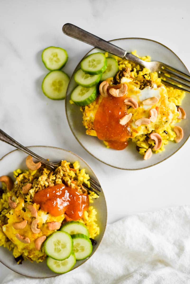 two plates with bobotie, yellow rice, cucumbers and apricot jam. Forks on the top of each plate.