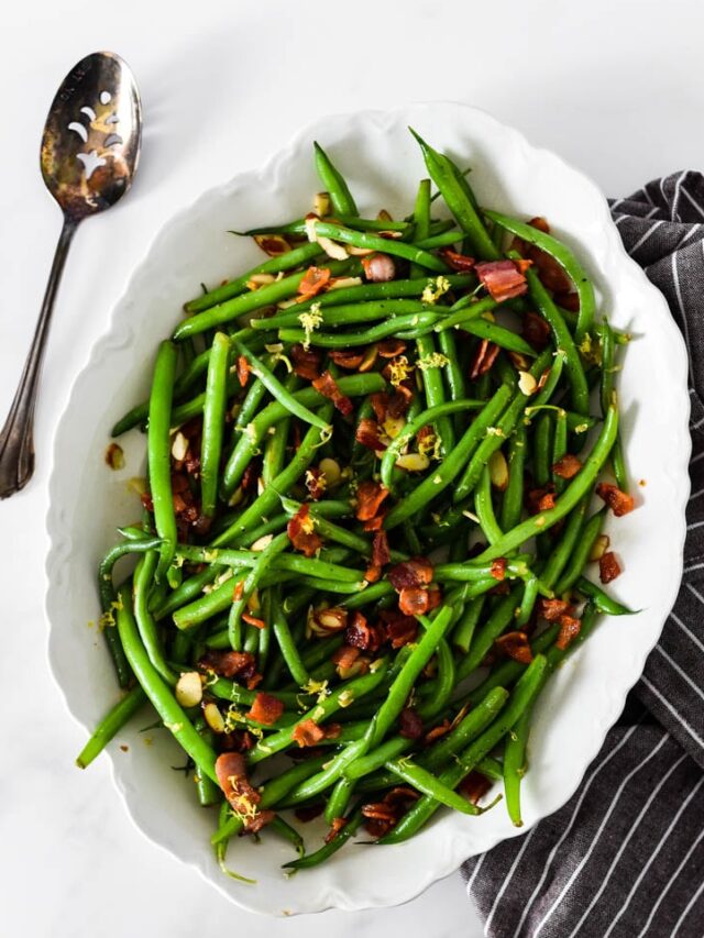 green beans almondine in white platter next to napkin and serving spoon