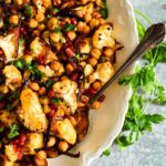 close up overhead view of roasted cauliflower with chickpeas onions and pomegranates on white platter with serving spoon to the side