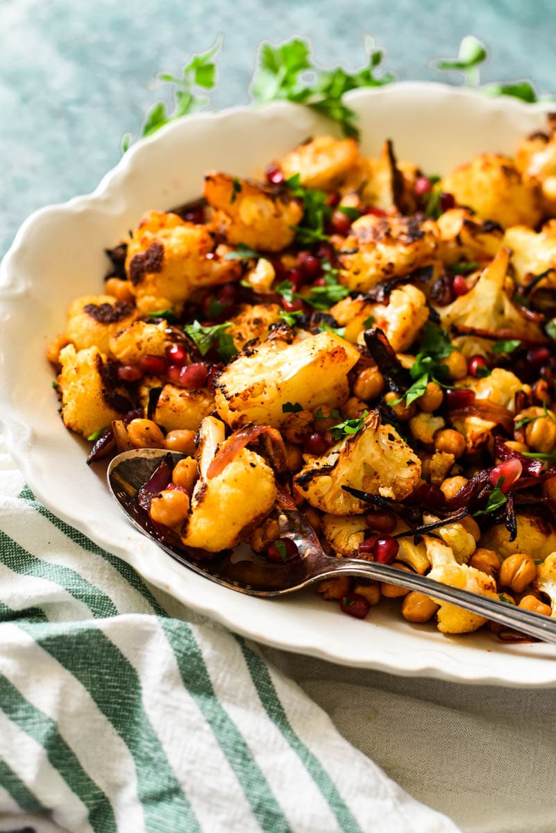 side view of white platter filled with roasted cauliflower topped with pomegranates and parsley