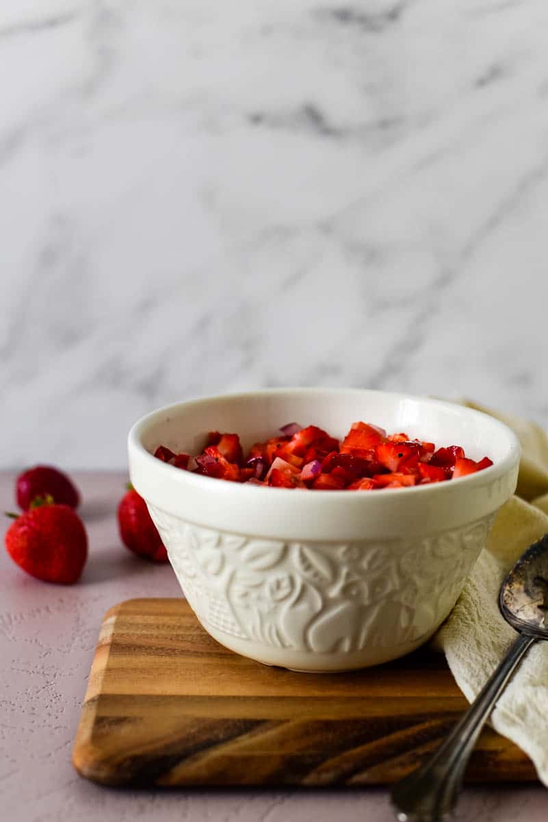 white serving bowl filled with fresh strawberry salsa on wood board