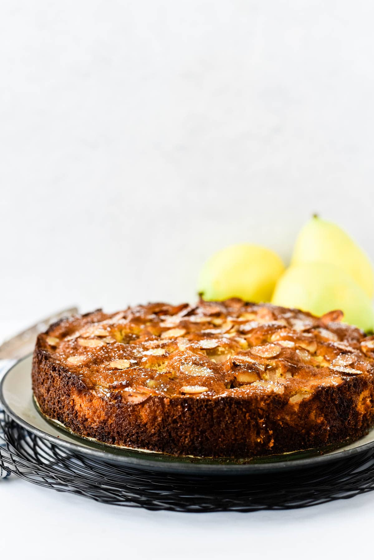 pear almond cake on platter with pears behind