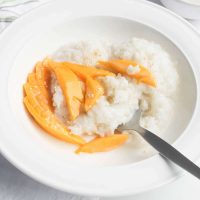 white bowl with spoon and rice and mango