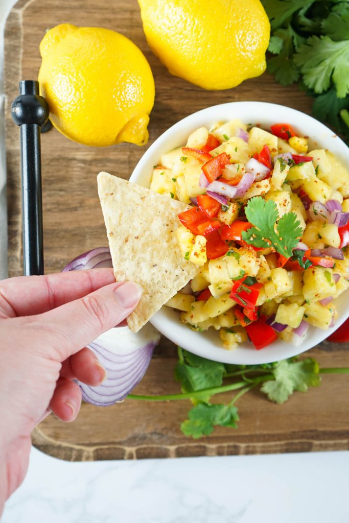 bowl with pineapple salsa and hand reaching in with chip
