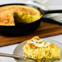 slice of cornbread on plate in front of cast iron skillet