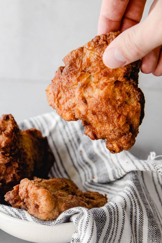 hand holding piece of fried chicken next to bowl
