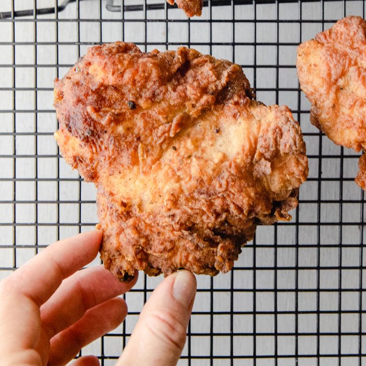 hand holding piece of fried chicken on cooling rack