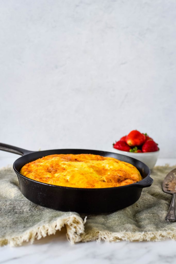 frittata in cast iron skillet with bowl of strawberries