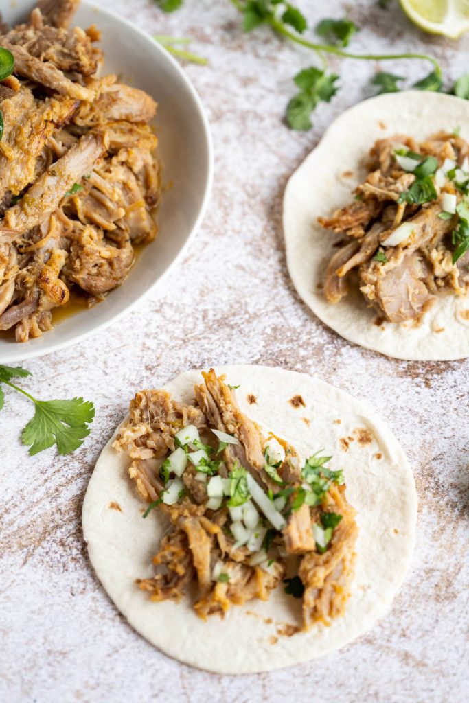 carnitas on flour taco shell with serving dish behind