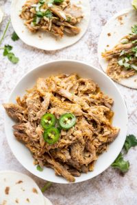 white serving bowl with carnitas and two tortillas behind