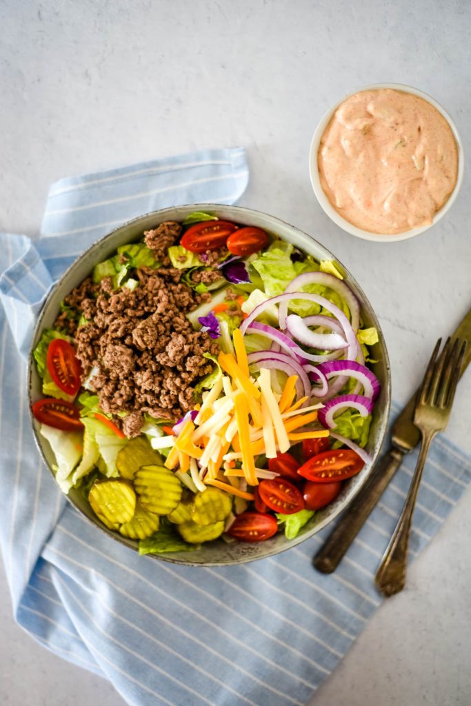 salad with ground beef and burger toppings of onions, cheese, tomatoes, pickles and special sauce dressing