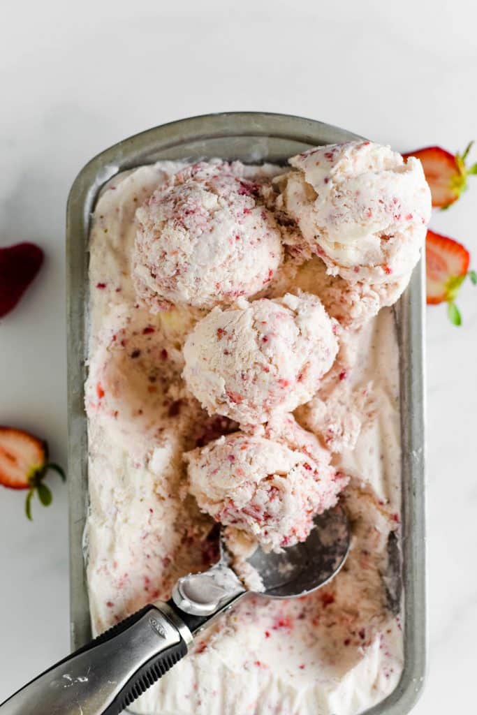 container with strawberry ice cream and scoop making scoops