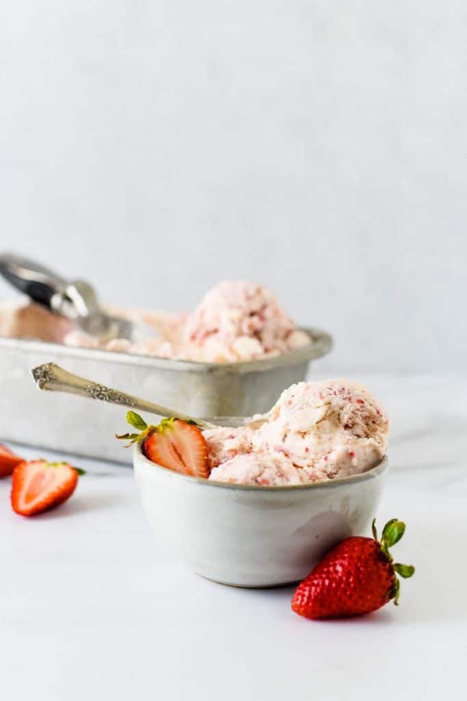 bowls of strawberry ice cream with sliced strawberries beside