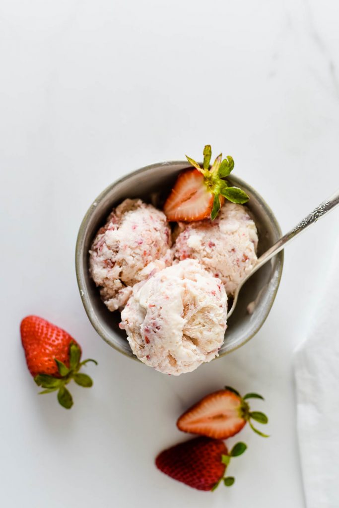 overhead view of bowl of strawberry ice cream with spoon and sliced strawberries beside