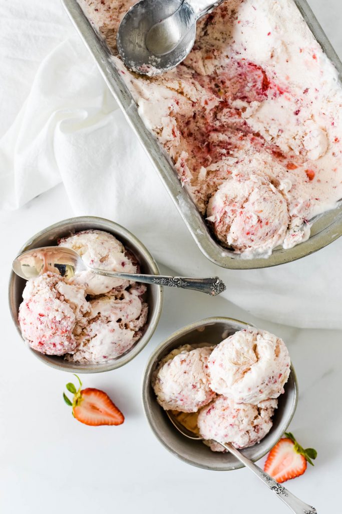 two bowls of strawberry ice cream next to filled container with scoop