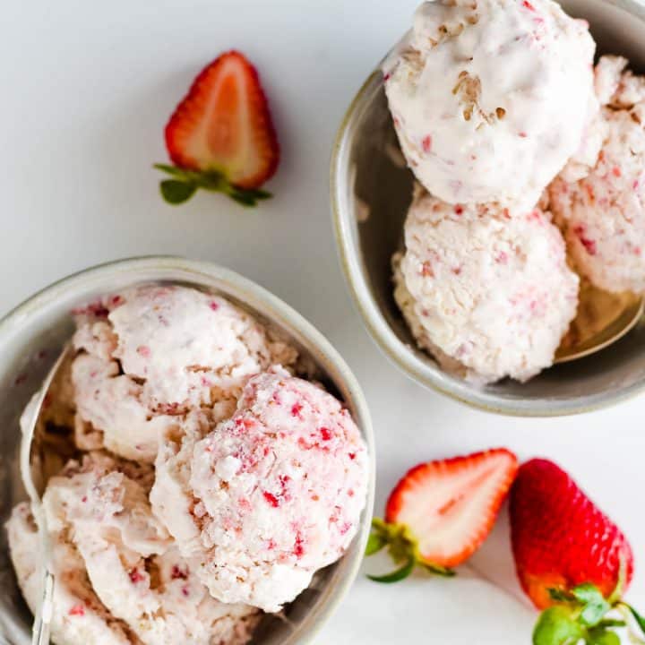 two bowls with scoops of strawberry ice cream and sliced strawberries beside
