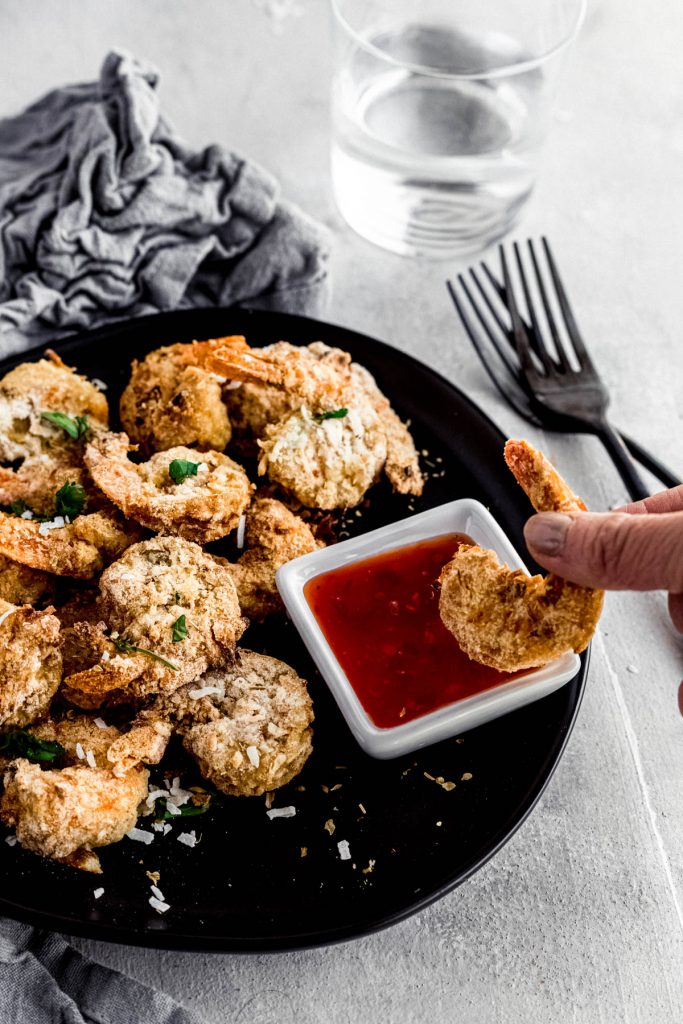 hand dipping coconut shrimp into chili sauce with platter behind