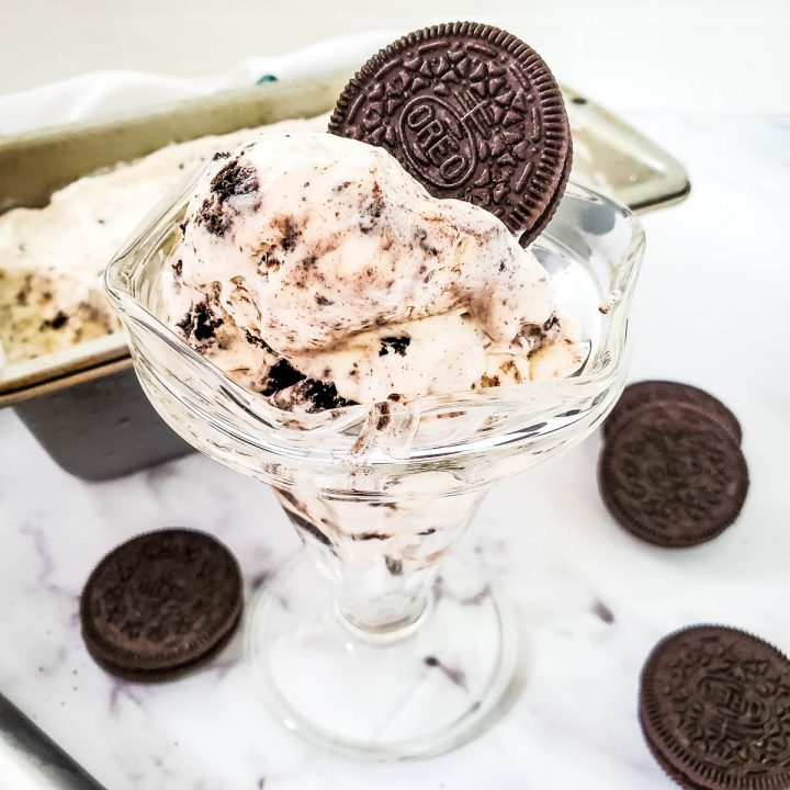 oreo ice cream in glass dish in front of container, surrounded by cookies