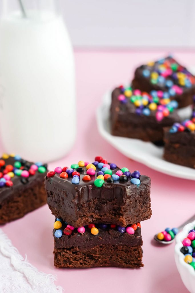 stacked brownies with bite out of top one, milk jar behind.