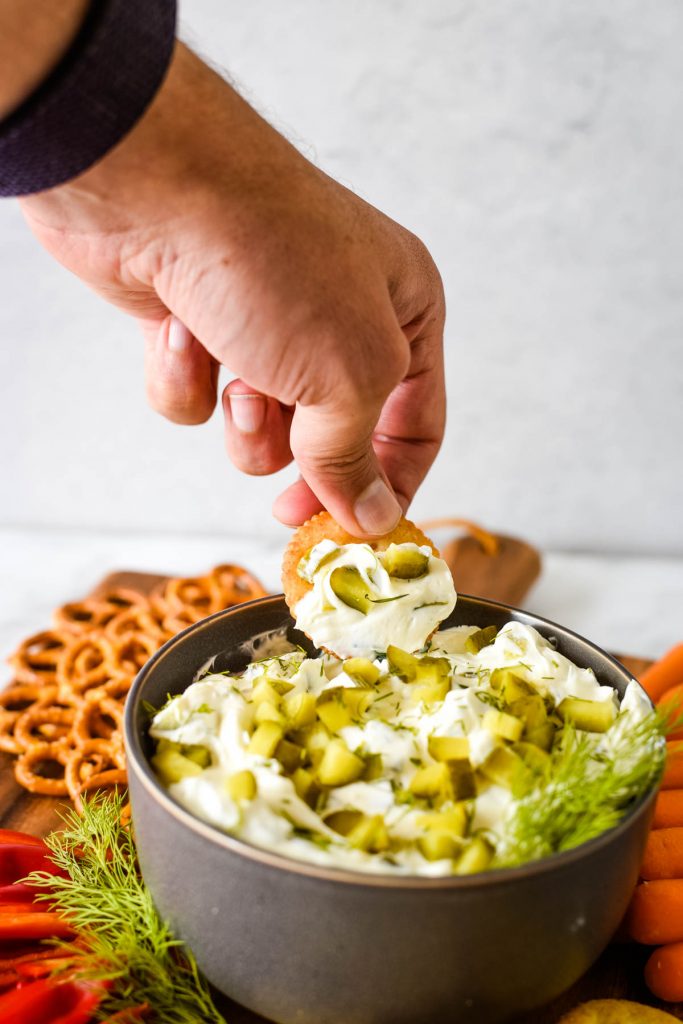 hand dipping cracker into pickle dip bowl