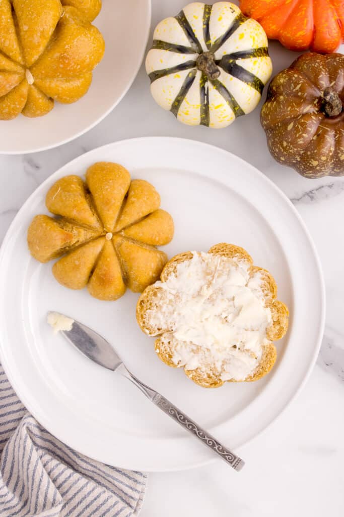 plate with two pumpkin rolls, one cut open with butter on it