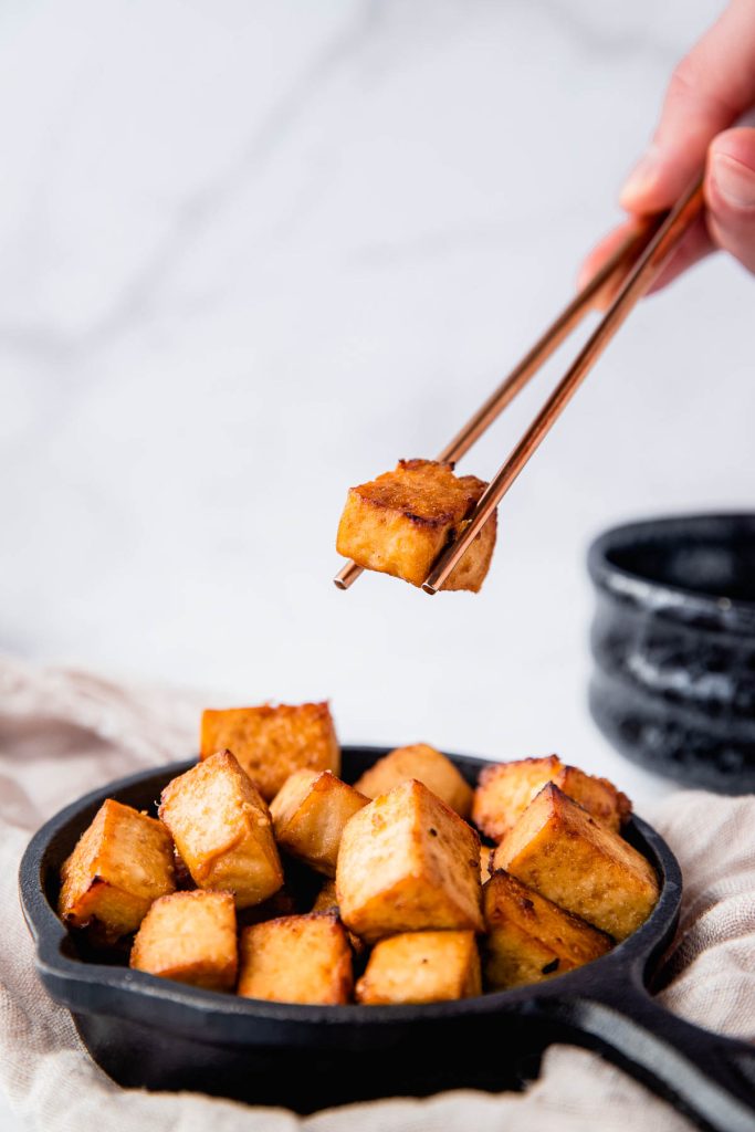 chopsticks holding tofu cube above platter