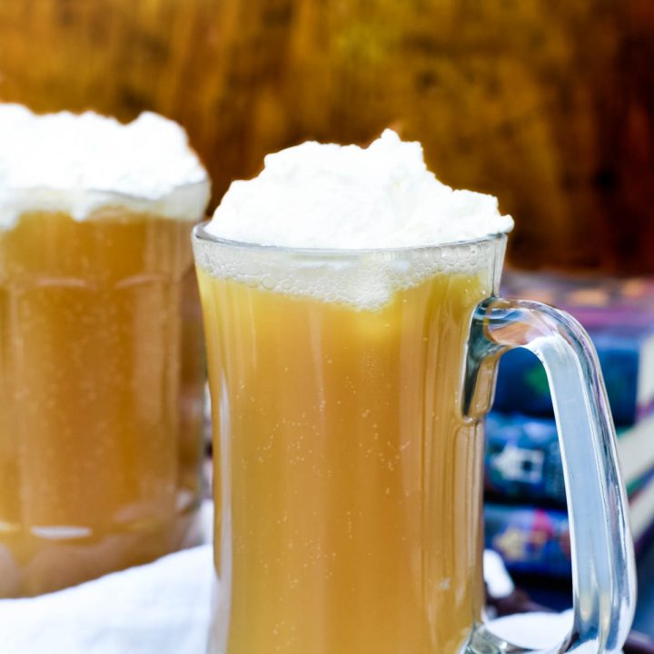 two mugs of butterbeer in front of stack of books