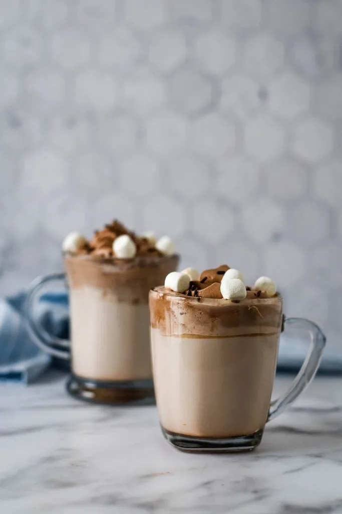 two glass mugs with whipped hot cocoa and marshmallows