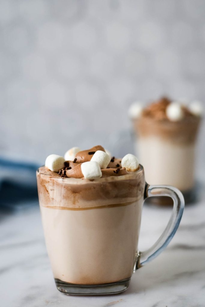 clear glass mug with hot milk and chocolate whipped cream