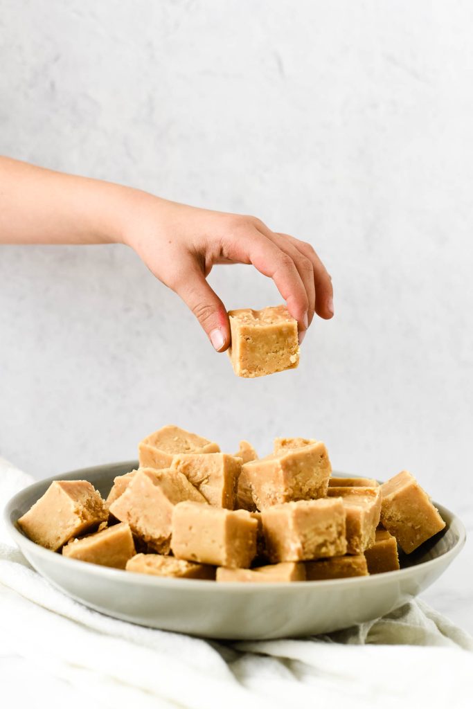 plate of peanut butter fudge squares with child hand removing one