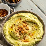 avocado hummus in bowl with crackers and spices behind