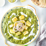 overhead view of bowl of palak paneer with cream and onions on top, flatbread beside