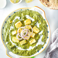 overhead view of bowl of palak paneer with cream and onions on top, flatbread beside