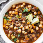 white bowl with lentil and chickpea soup with limes on top