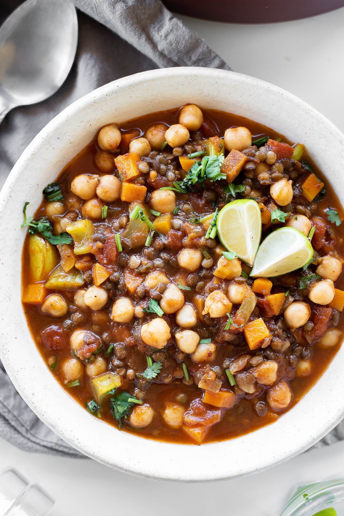 white bowl with lentil and chickpea soup with limes on top