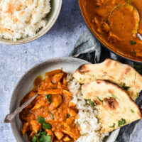 bowl with curry, rice and naan next to serving bowls