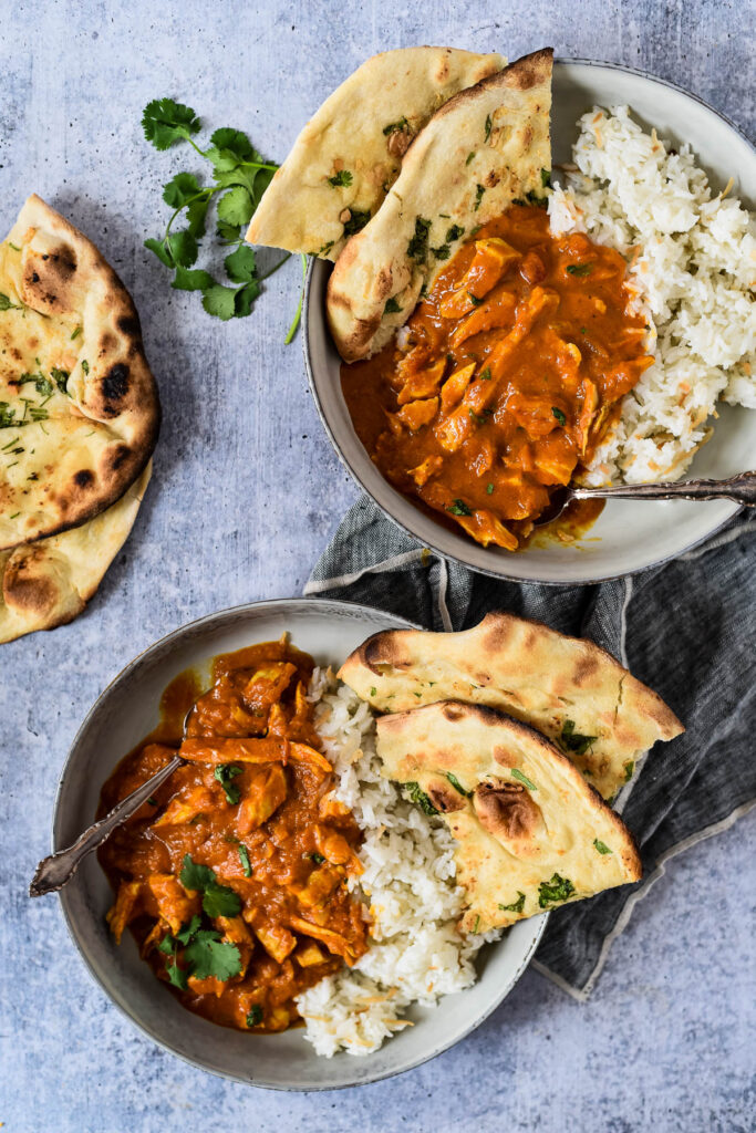 turkey curry in two bowls with rice and naan